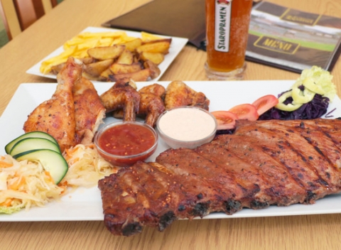 Kilové pečené bravčové rebrá s chlebom, kuracími krídelkami, hranolkami a pečenými zemiakmi.